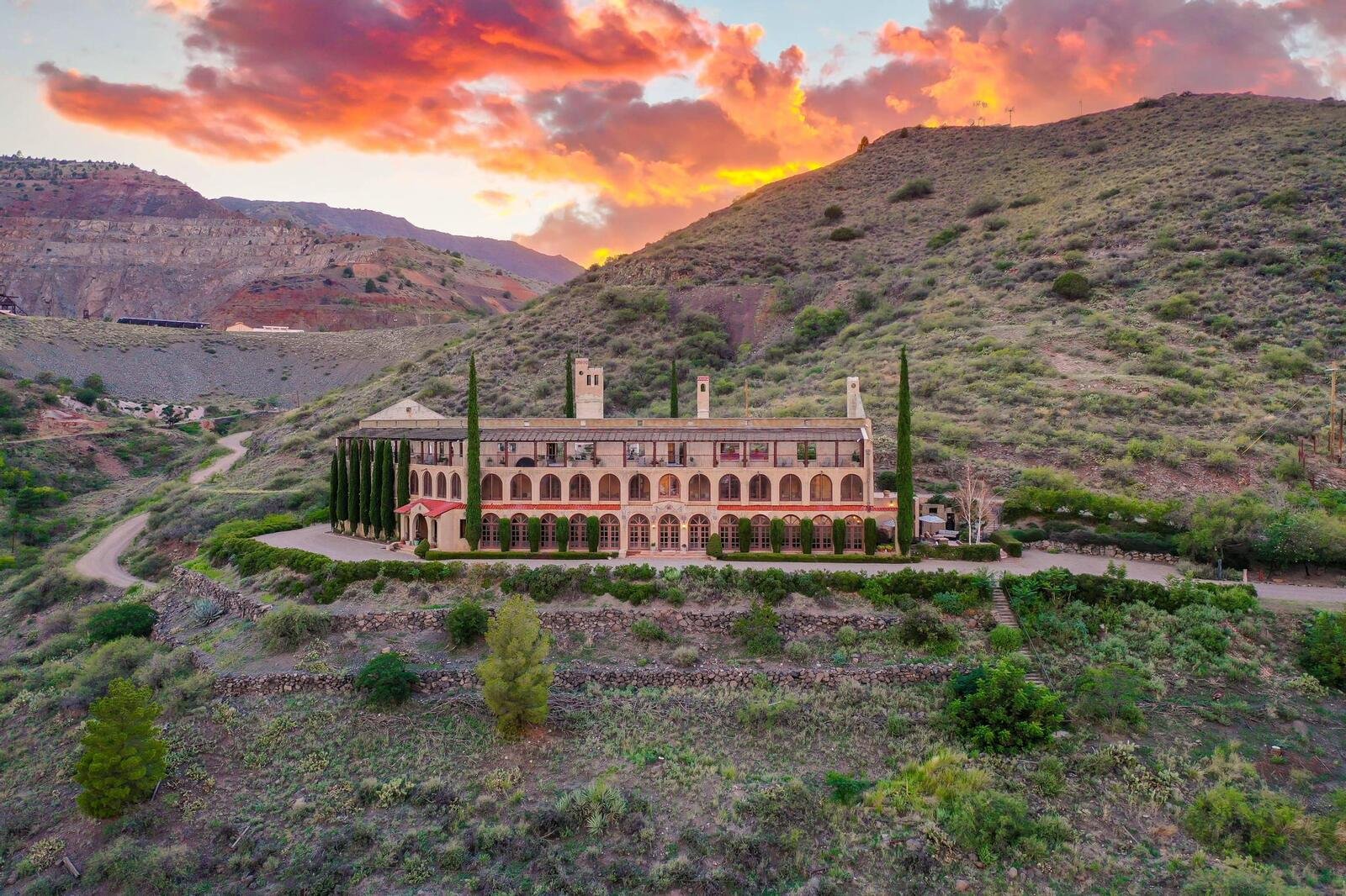 Aerial view of The Little Daisy, a historic luxury event venue in Jerome, Arizona, with arched facade and cypress trees against a hillside at sunset